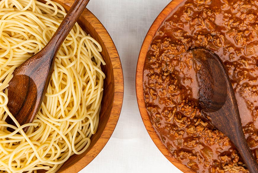 A close-up of a traditional Greek pastitsio dish, a baked pasta casserole topped with creamy béchamel sauce, served in a rustic wooden bowl.